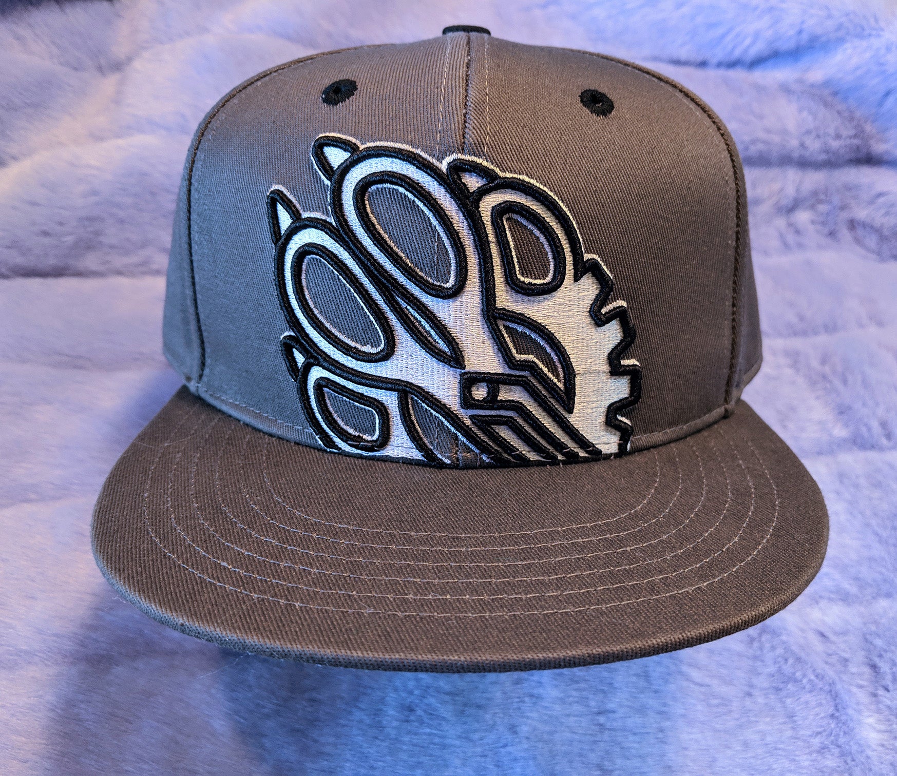 Gray cap with a black and white Fuzz Factory on a fur background