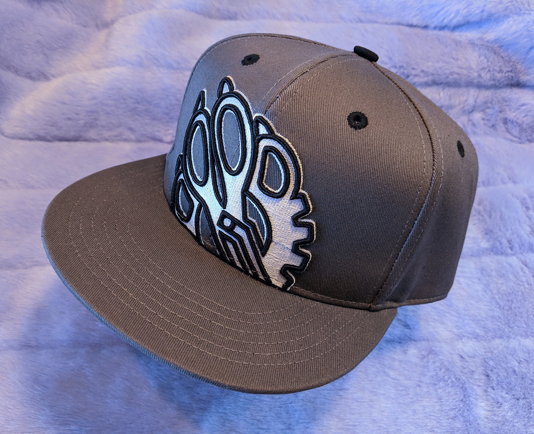 Gray cap with a black and white Fuzz Factory logo on a fur surface