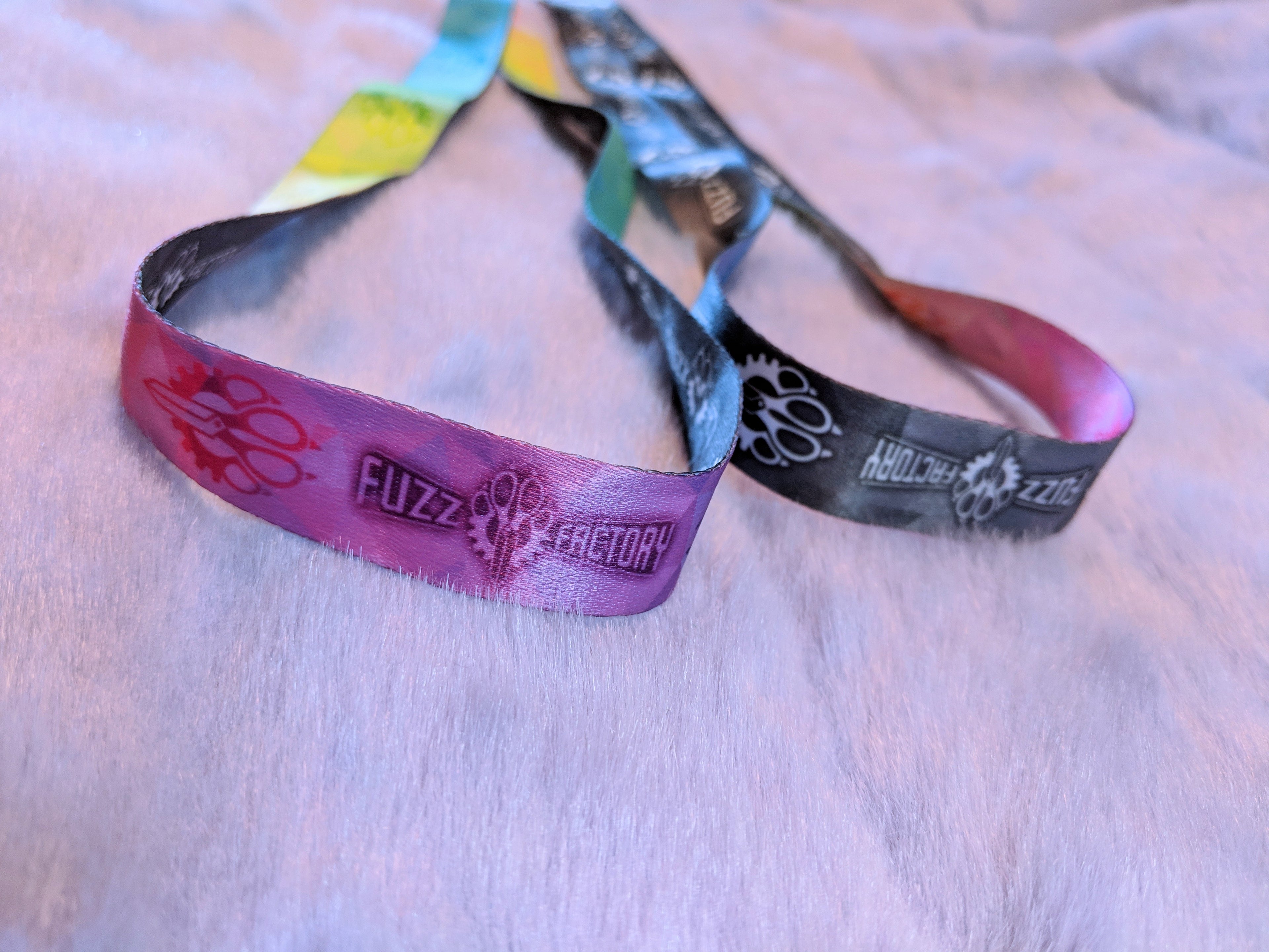 Two colorful wristbands with 'Fuzz Factory' branding on a light background