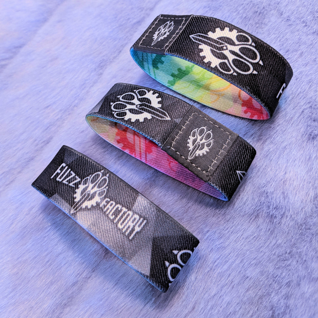 Three wristbands with 'Fuzz Factory' branding with the monochrome side out on a fur surface.